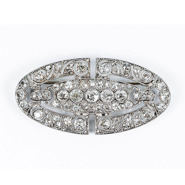 Bello alfiler oval de época art-decó, en platino y limpios y blancos diamantes, con motivo en fila central de brillantes talla antigua