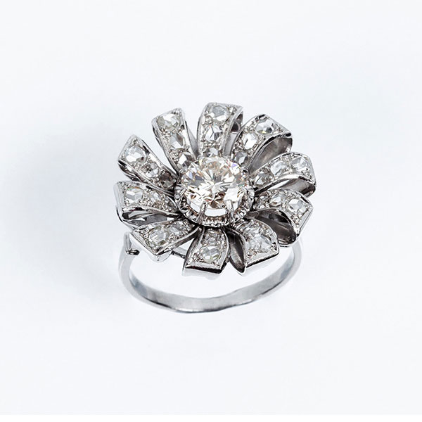 Bella sortija vintage en forma de flor, en platino, con un limpio y blanco diamante central, talla brillante orlado en 'pétalos' cuajados de diamantitos 