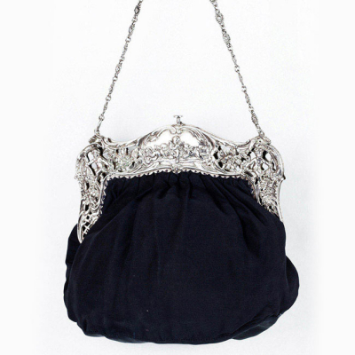 Bolso de mano vintage en plata y tela negra, con decoración calada estilo rococó, con motivos de flores y angelotes.