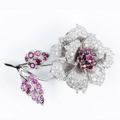 Un gran alfiler en forma de flor, en oro blanco, cuajado de rubíes en garritas, y limpios y blancos diamantitos talla brillante en pavé
