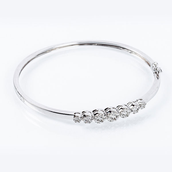 Brazalete esclavo en sólida montura de oro blanco 18 K, con motivo central de siete rosetones de limpios y blancos diamantes naturales 