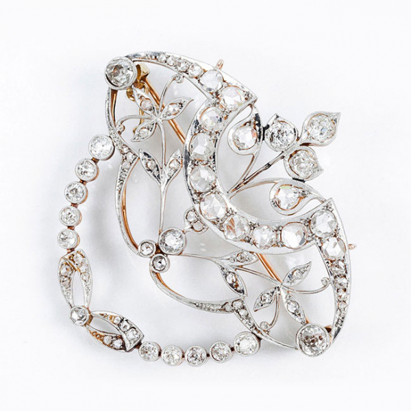 Delicado alfiler-centro colgante 'art-nouveau', de época modernista, en montura calada de oro amarillo con formas vegetales cuajadas de limpios y blancos diamantes talla simple, rosa y brillantes talla antigua sobre vistas grafiladas de platino.