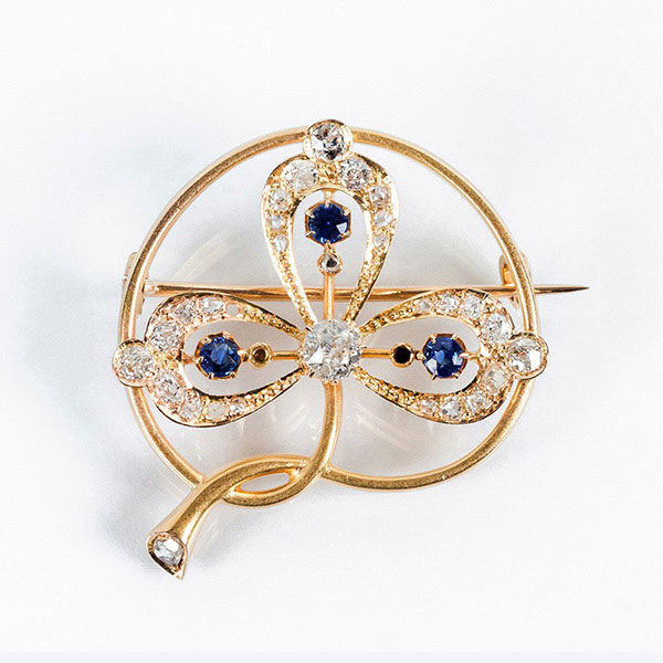 Bello alfiler de autor, &eacute;poca modernista, en oro amarillo 18 K tr&eacute;bol con diamante central, talla brillante antigua y zafiros azules.