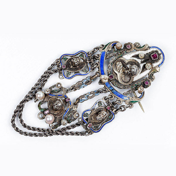 Gran alfiler pinjante antiguo, realizado en plata, en motivo calado con busto y cabezas sobresalientes de personajes, colgantes, con decoraci&oacute;n de esmaltes (varias faltas), rubelitas y perlitas y doble cord&oacute;n. S XVIII-XIX.