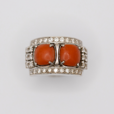 Sortija en oro blanco con dos cabujones de coral engastados en garras y ornamentada con diamantes talla brillante.