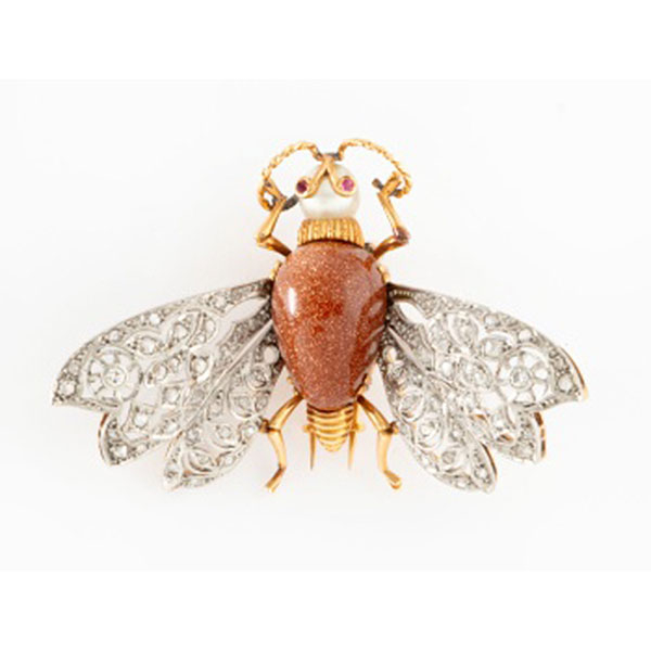 Broche representando mosca en oro amarillo y alas en oro blanco con cuerpo en piedra venturina, perla cultivada representando cabeza, y rubís en los ojos, alas con decoración de flores con 2 diamantes talla brillante y cuajado de diamantes.