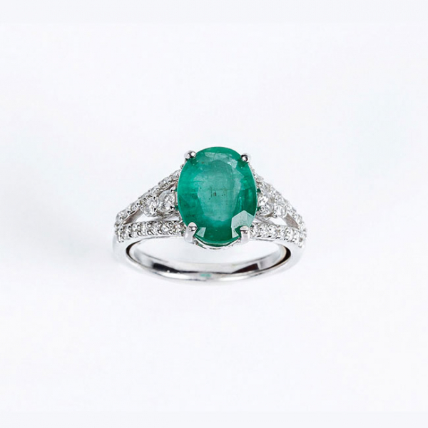 Sortija en oro blanco 18 K con una bonita esmeralda natural, talla oval, flanqueada de limpios y blancos diamantes 