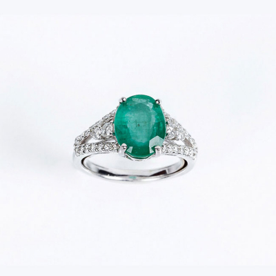 Sortija en oro blanco 18 K con una bonita esmeralda natural, talla oval, flanqueada de limpios y blancos diamantes 
