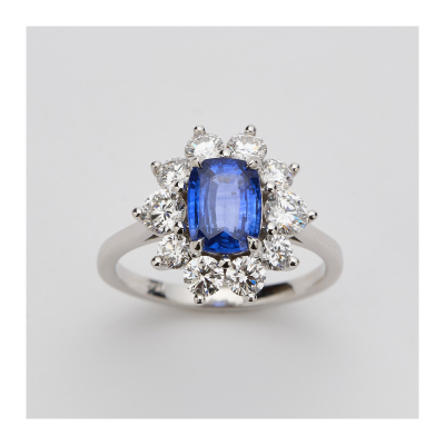 Sortija rosetón en oro blanco con zafiro azul talla oval orlado por diamantes talla brillante.