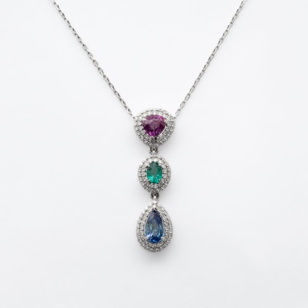 Gargantilla en oro blanco con tres rosetones de rub&iacute; talla trill&oacute;n, esmeralda talla oval y zafiro azul talla perilla orlados por dos bandas de diamantes talla brillante.