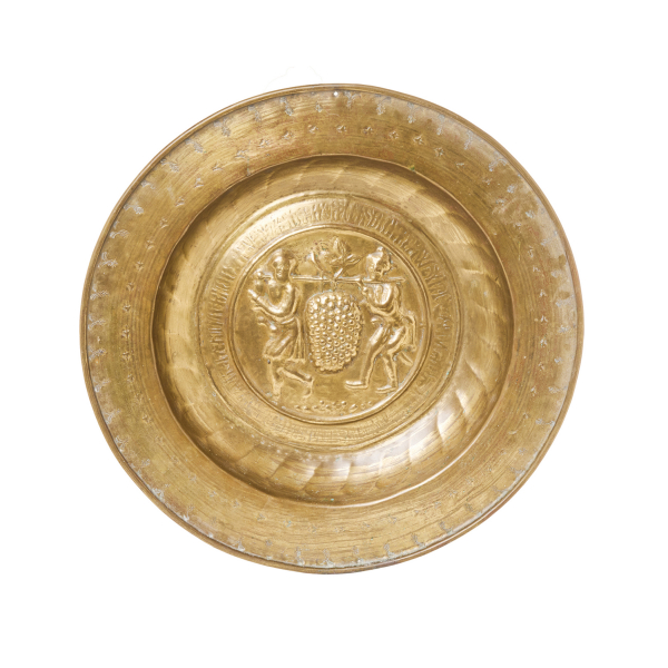 Plato petitorio de limosna en lat&oacute;n repujado con decoraci&oacute;n central de escena con los esp&iacute;as de Canaan, Josua y Caleb portando las uvas custodiada por cenefa con letras g&oacute;ticas, N&uacute;remberg, Alemania, s.XV.