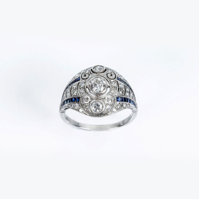 Delicada sortija estilo art-decó en platino, con un limpio y blanco diamante central y bandas de zafiros finos azules 