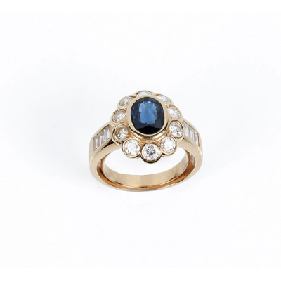 Sortija en s&oacute;lida montura de oro amarillo 18 K con zafiro fino azul, oval, en chat&oacute;n, y orla en fila de limpios y blancos diamantes, 