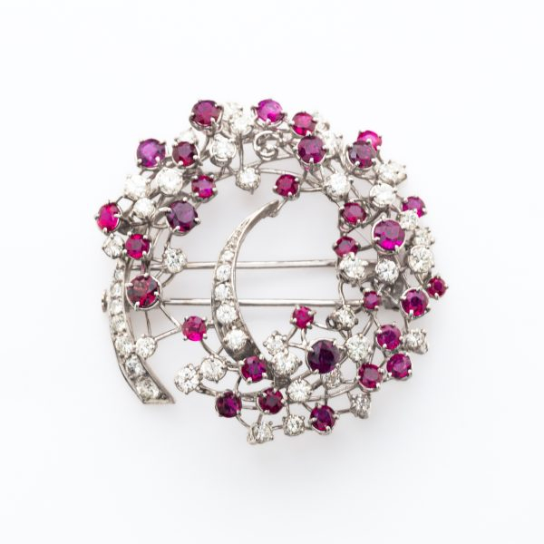 Broche calado estilo corona floral en oro blanco cuajado de diamantes talla brillante y rub&iacute;es talla redonda engastados en garras.