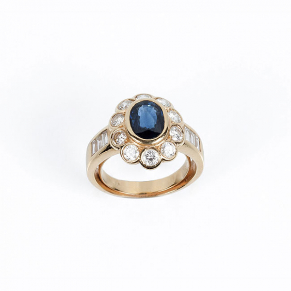 Sortija en oro amarillo 18 K con zafiro fino azul, oval, en chatón, y orla en fila de limpios y blancos diamantes