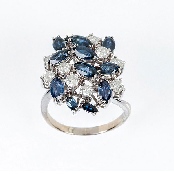 Sortija vintage en sólida montura de oro blanco 18 K con motivo en gran penacho de limpios y blancos diamantes, talla brillante y zafiros finos azules, talla marquisse, salteados a diferentes alturas, en garras