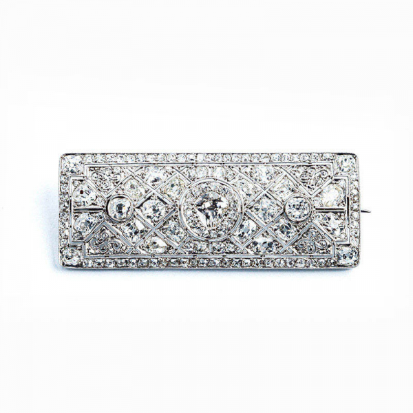 Espléndido broche antiguo, &#039;art-decó&#039;, en platino, cuajado de blancos diamantes talla brillante antigua, y talla &#039;cojín&#039;, en decoración grafilada, con un limpio y blanco diamante central, talla oval