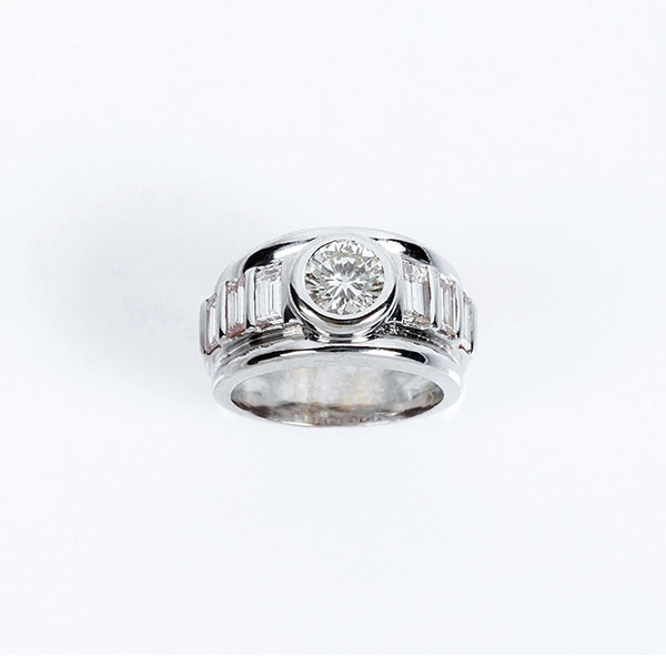 Sortija de alta joyer&iacute;a en s&oacute;lida montura de oro blanco con un limpio y blanco diamante, talla brillante central, en chat&oacute;n, entre bandas de limpios y blancos diamantes talla baguette