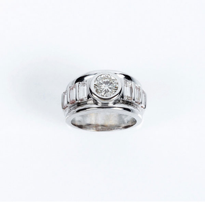 Sortija de alta joyer&iacute;a en s&oacute;lida montura de oro blanco con un limpio y blanco diamante, talla brillante central, en chat&oacute;n, entre bandas de limpios y blancos diamantes talla baguette