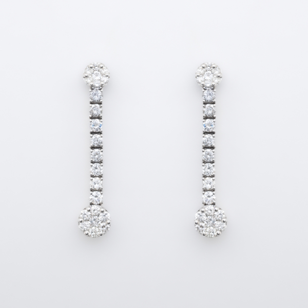 Pendientes largos en oro blanco con dos rosetones unidos por l&iacute;nea de diamantes talla brillante.