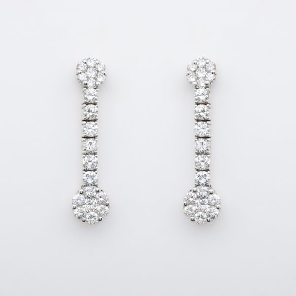 Pendientes largos en oro blanco con dos rosetones unidos por línea de diamantes talla brillante.