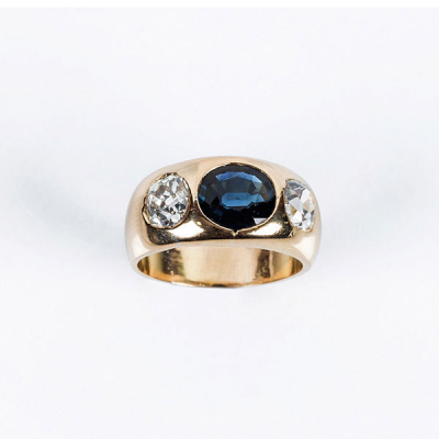 Sortija vintage en sólida montura de oro amarillo 18 K, con un zafiro fino azul oval (1.80 ct aprox.), entre dos limpios y blancos diamantes, talla cojín antigua