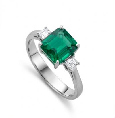 Sortija en oro blanco con esmeralda central y 2 diamantes talla princesa laterales con un peso total de 0,25 cts.