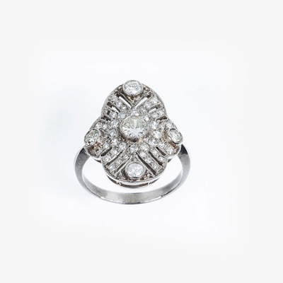 Bella sortija lanzadera art-decó en platino cuajada de limpios y blancos diamantes, talla brillante y 8/8. Tiene un brillante central y cuatro centros periféricos en chatón, sobre patrón calado, oval, en decoración grafilada