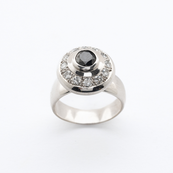 Sortija diseño circular en oro blanco con un diamante negro talla brillante orlado por diamantes talla brillante.