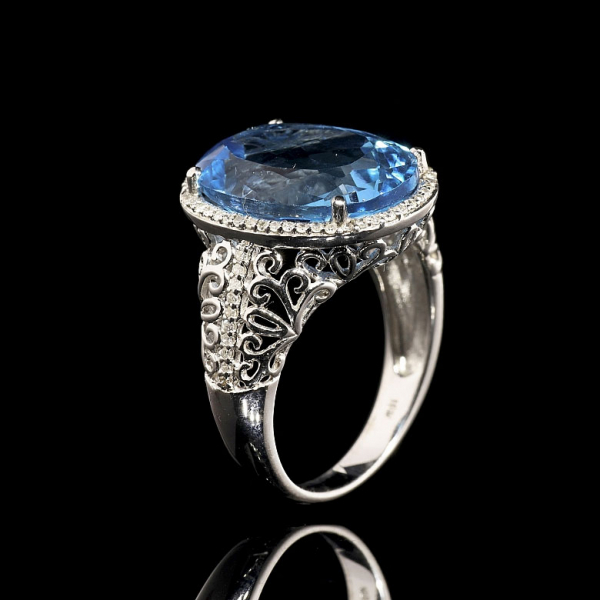 Anillo con topacio y diamantes en oro blanco de 18 kt.    Anillo de oro blanco 18 kt con una cenefa recortada y un dibujo de flor de lis.