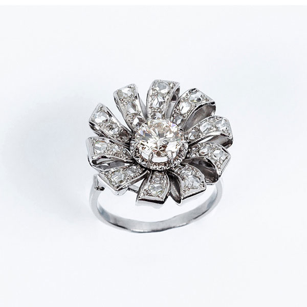 Bella sortija vintage en forma de flor, en platino, con un limpio y blanco diamante central, talla brillante orlado en 'pétalos' cuajados de diamantitos simples en decoración grafilada