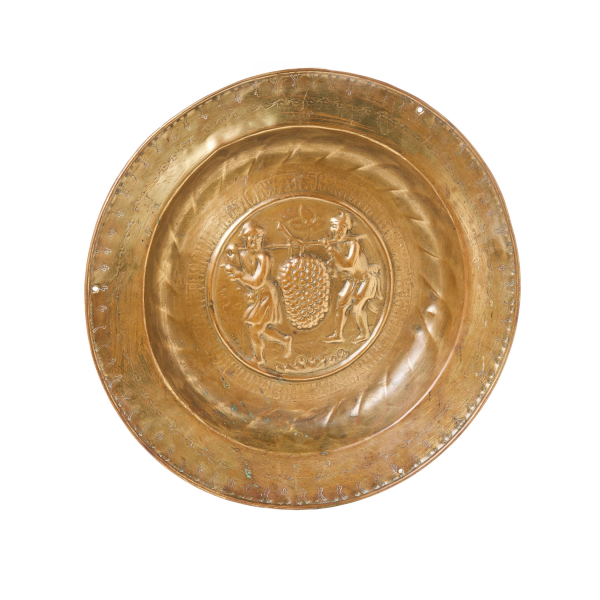 Plato petitorio de limosna en lat&oacute;n repujado con decoraci&oacute;n central de escena con los esp&iacute;as de Canaan, Josua y Caleb portando las uvas custodiada por cenefa con letras g&oacute;ticas, N&uacute;remberg, Alemania, s.XV.