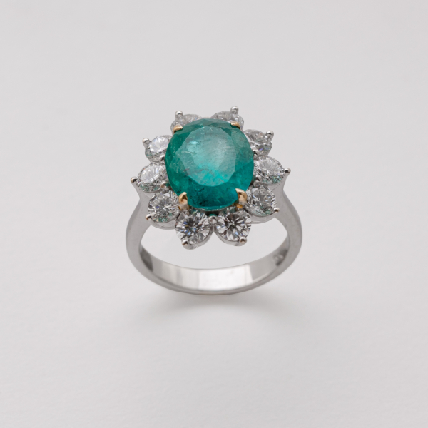 Sortija rosetón en oro blanco con esmeralda colombiana talla oval orlada por diamantes talla brillante.