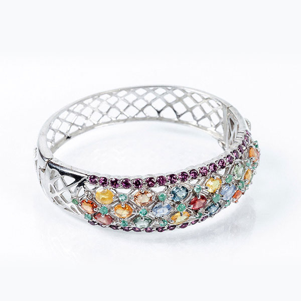 Brazalete esclavo en de plata de ley, con celosía calada y frente cuajado de zafiros finos de colores, ovales, en garritas, entre bandas en fila de zafiros rosas.