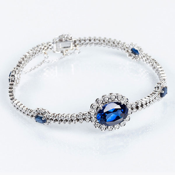 Brazalete vintage en oro blanco 18 K formado por doble fila riviere con limpios y blancos diamantes, talla brillante, y rosetones con centro de zafiro fino azul oval