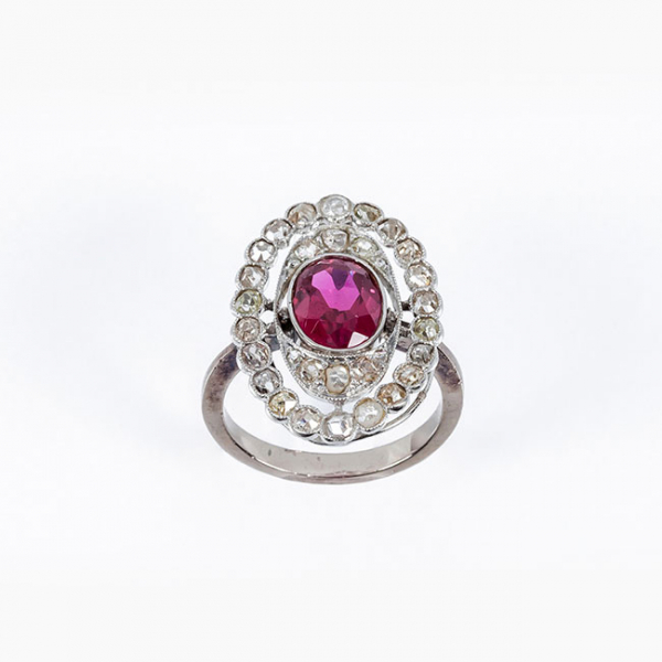 Sortija lanzadera estilo art-decó en oro blanco 18 K, con una piedra roja, talla oval central, y doble orla calada de diamantes 