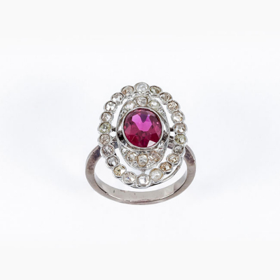 Sortija lanzadera estilo art-dec&oacute; en oro blanco 18 K, con una piedra roja, talla oval central, y doble orla calada de diamantes 