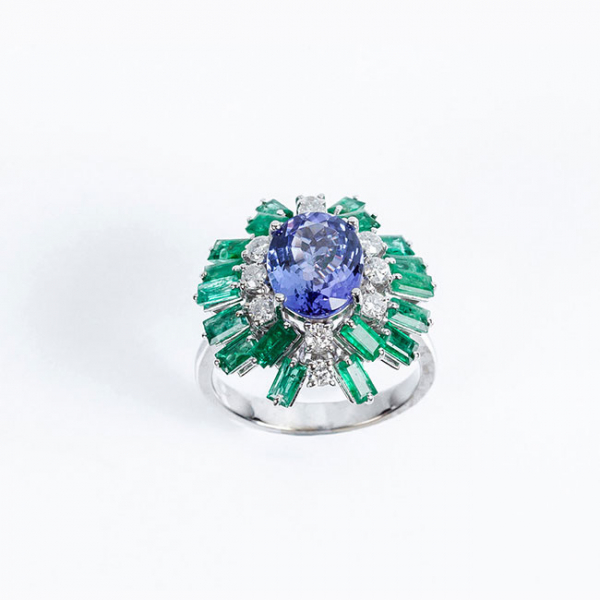 Sortija en oro blanco con una bella tanzanita oval orlada de limpios y blancos diamantes, talla brillante y bonitas esmeraldas