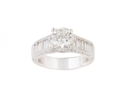 Sortija solitario de 2 ct en montura decorada con diamantes talla baguette en el frente y brillantes en laterales. En oro blanco de 18K.